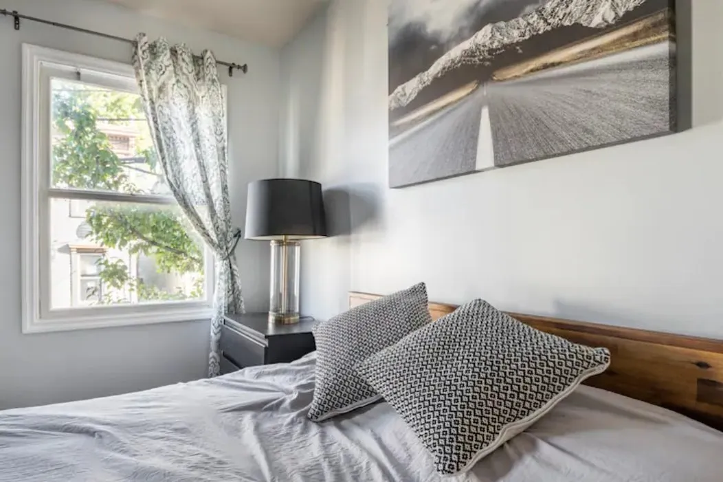 Bedroom with a wooden headboard and patterned cushions beside a window