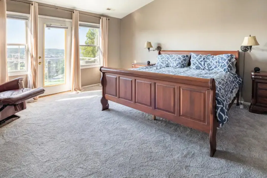 Bedroom with a wooden sleigh bed and windows looking out over the city